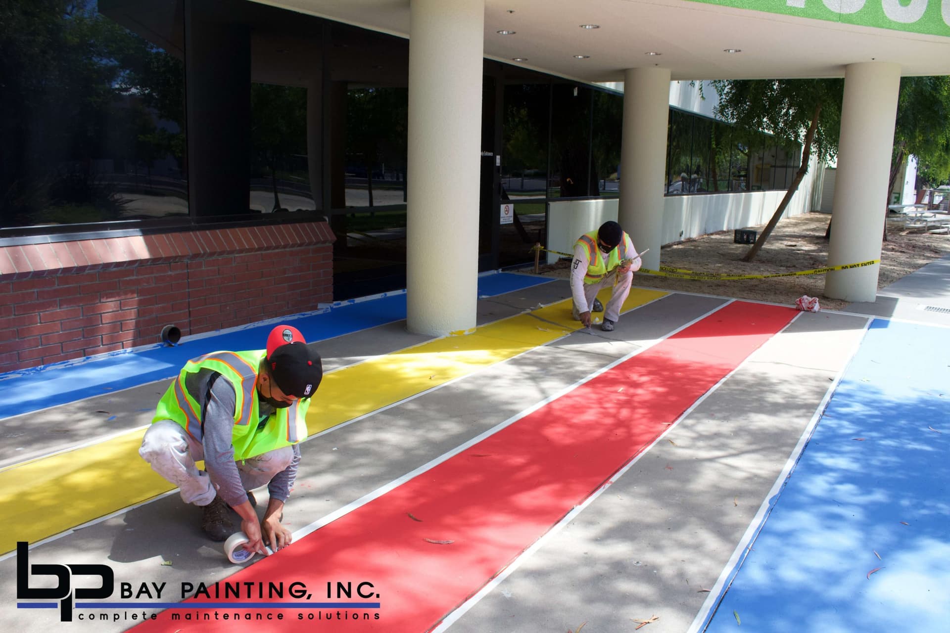 Bay Painting crew painting a multi-color striped crosswalk at a commercial building entrance
