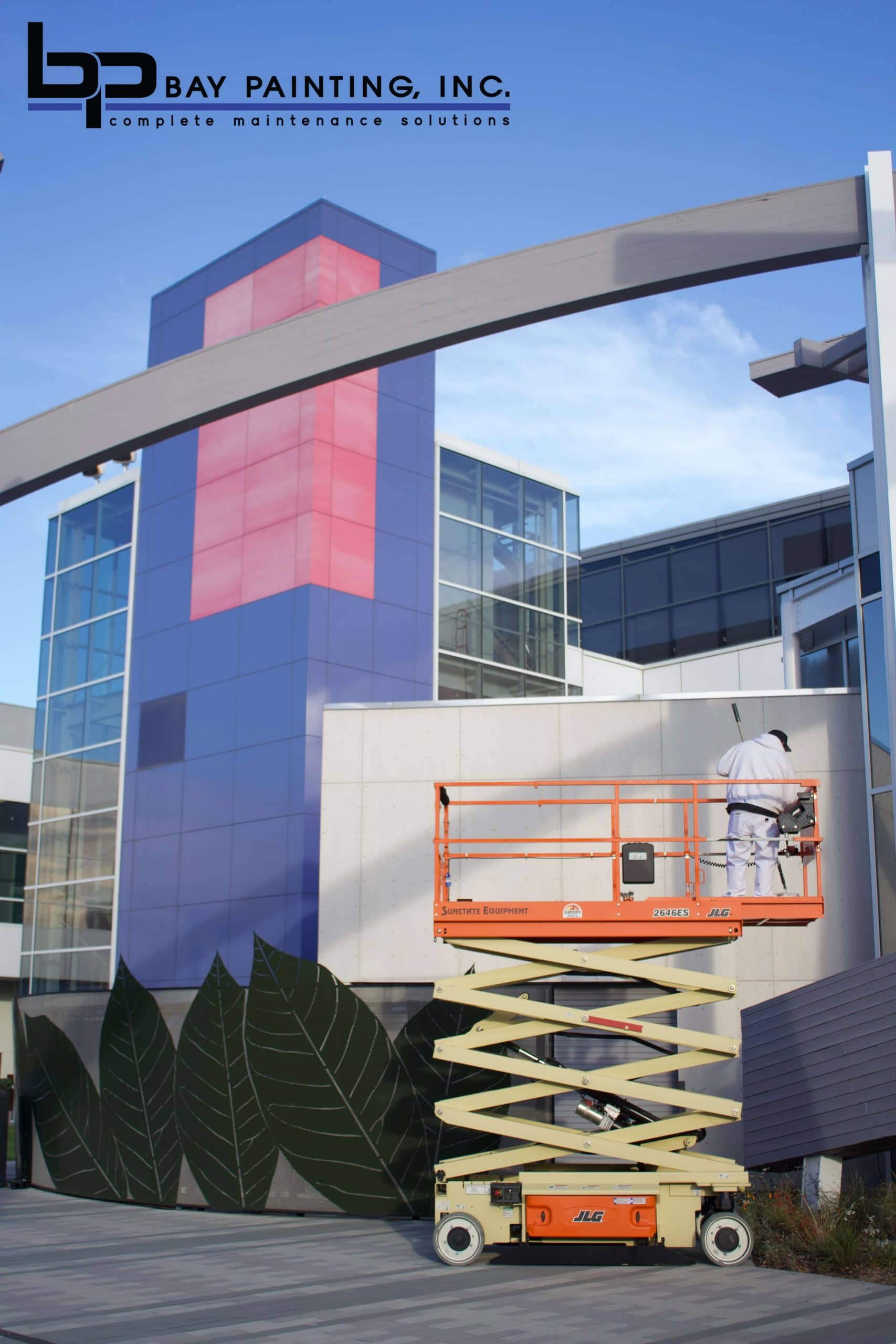 Bay Painting crew member on a scissor lift painting a commercial building facade