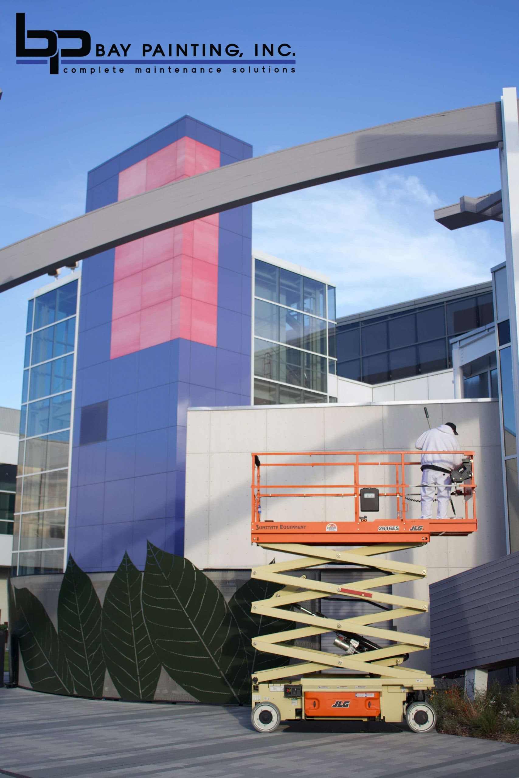 Bay Painting crew member on a scissor lift painting a multi-story commercial building facade