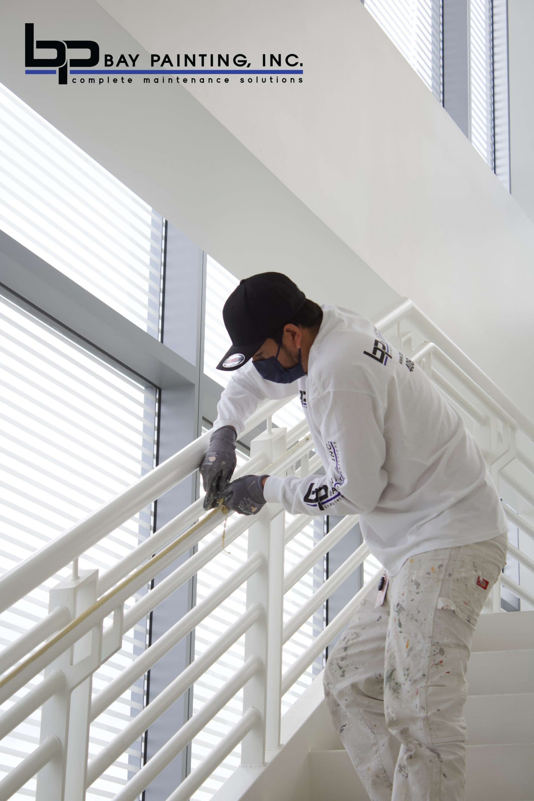 Bay Painting crew member painting a stairwell handrail in a commercial office building