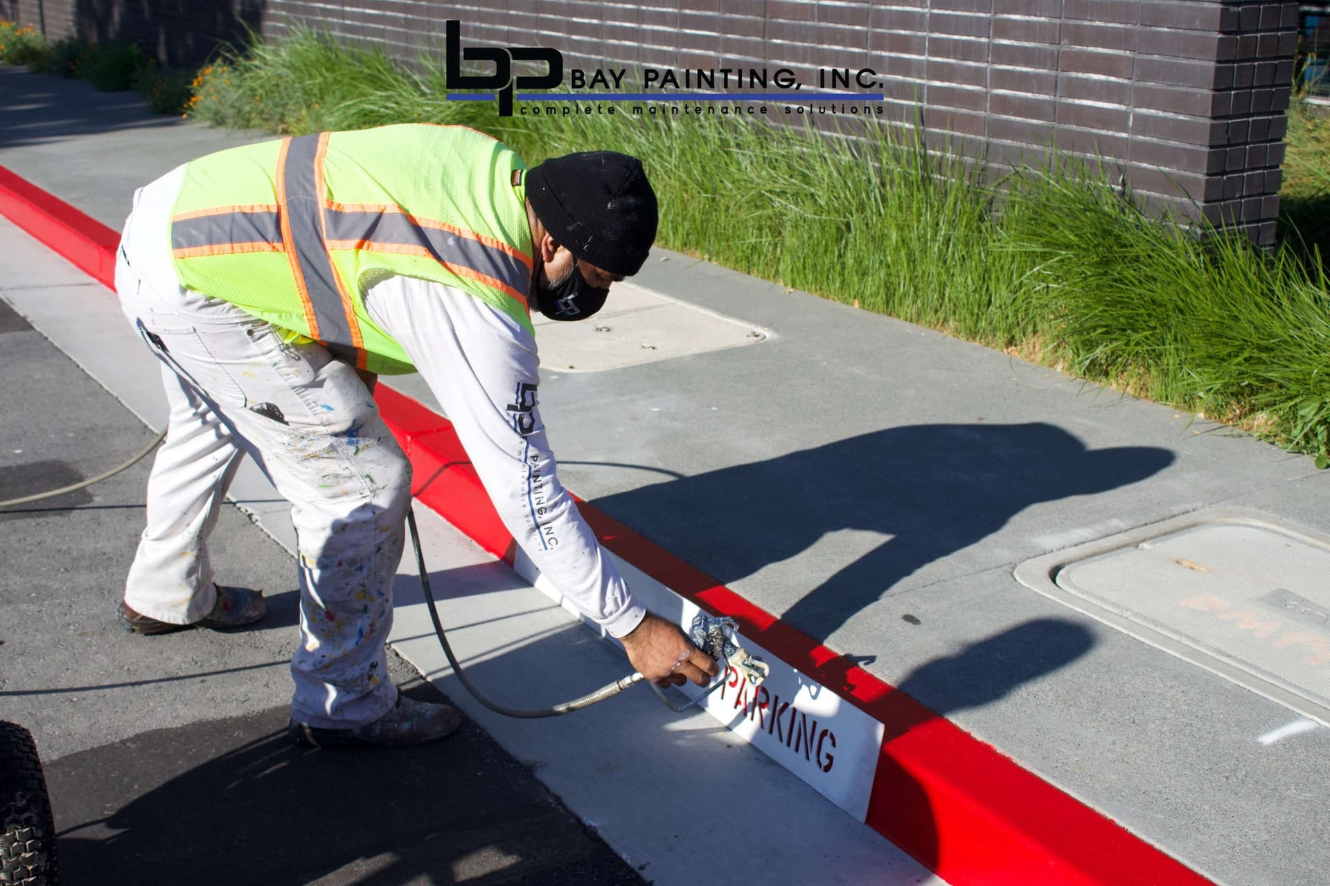 Bay Painting crew member stenciling a parking sign on a painted curb wheel stop