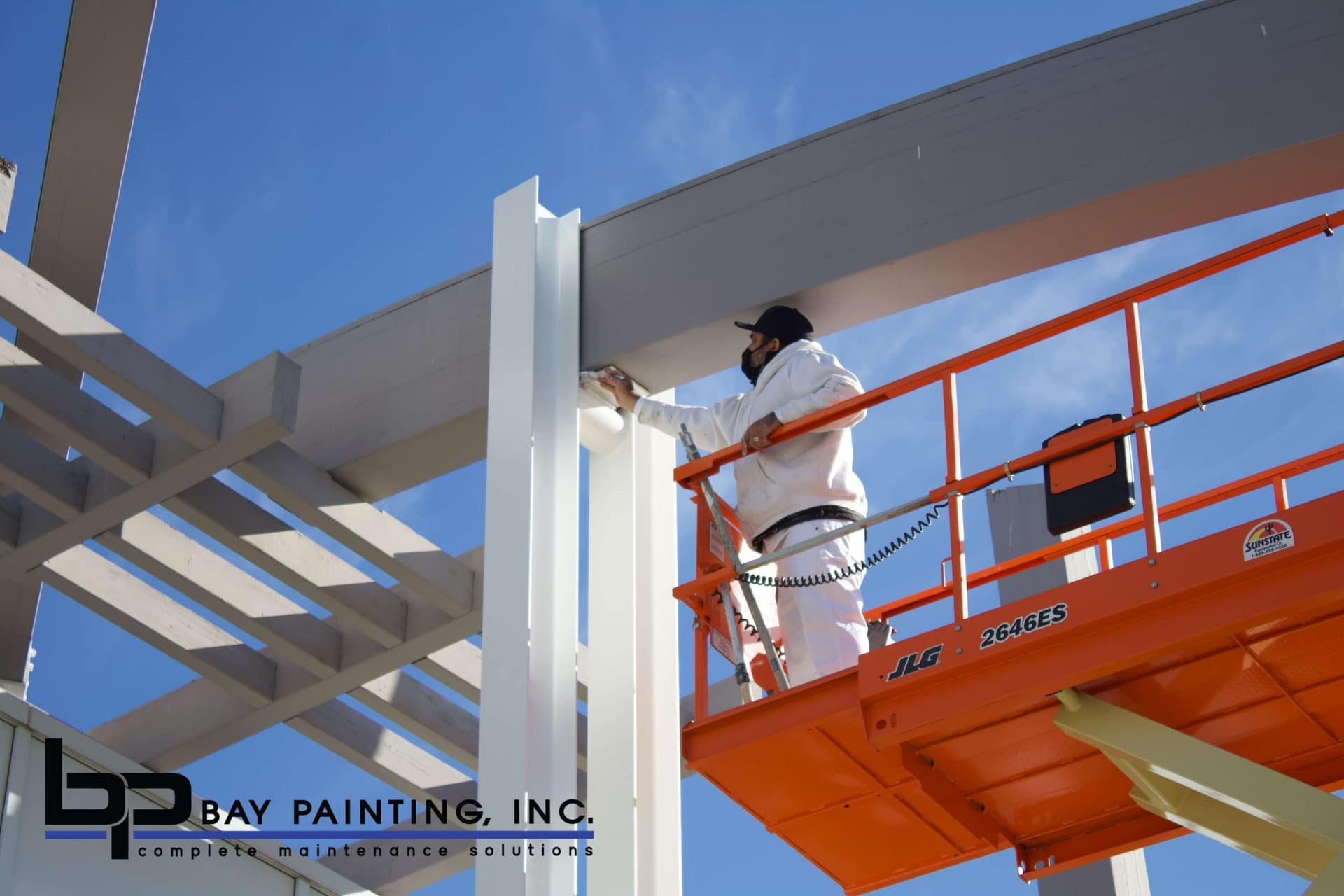 Bay Painting crew member painting an exposed structural steel beam from a scissor lift
